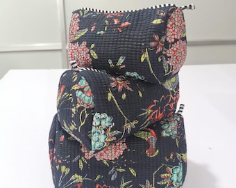 May include: Three stacked navy blue cosmetic bags with a floral pattern in pink, red, yellow, and teal. The bags have a quilted texture and a black and white striped zipper. The bags are on a white surface.