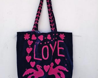 May include: A navy blue tote bag with pink embroidered details. The bag features the word "LOVE" in large letters, along with pink hearts, flowers, and two birds. The handles are also embroidered with a pink leaf design.
