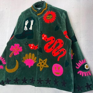 May include: A dark green velvet jacket featuring colorful embroidered patches including a cowboy boot, a red snake, a bright pink flower, a yellow crescent moon, a gold star, a pink smiley face, a sun, and an eye with pink eyelashes.