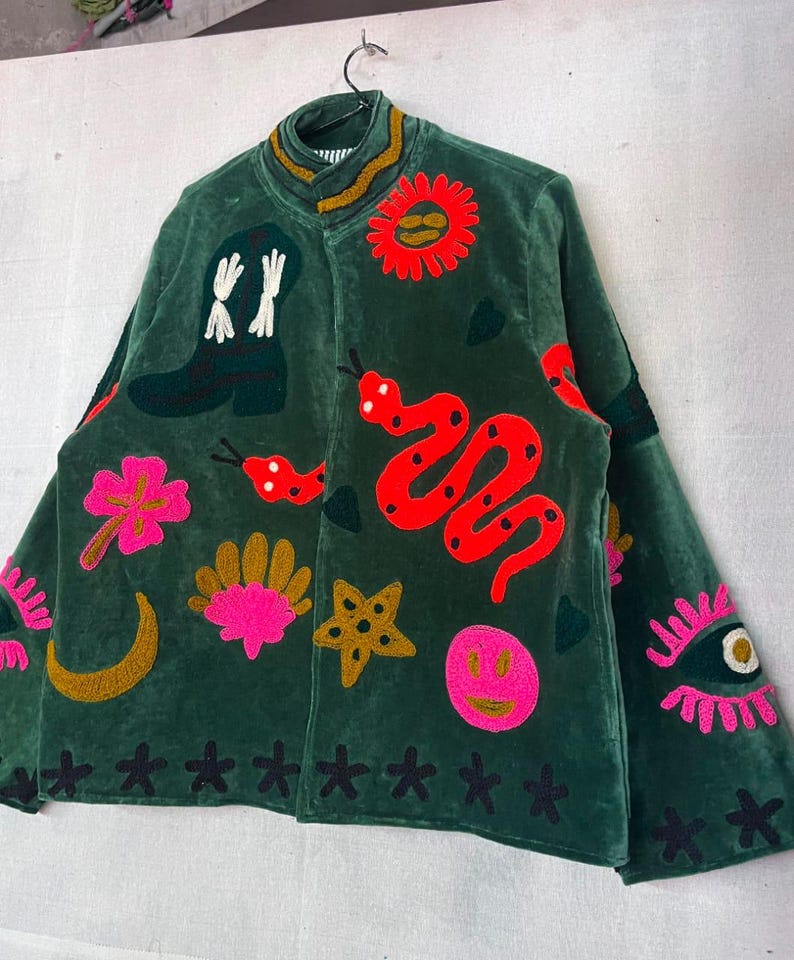 May include: A dark green velvet jacket featuring colorful embroidered patches including a cowboy boot, a red snake, a bright pink flower, a yellow crescent moon, a gold star, a pink smiley face, a sun, and an eye with pink eyelashes.