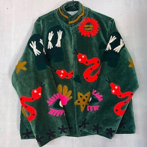 May include: A dark green velvet jacket featuring vibrant embroidered motifs including bright red snakes, yellow stars, pink eyes, and white abstract shapes. The jacket has a high collar, long sleeves, and a front zipper closure with a striped lining.