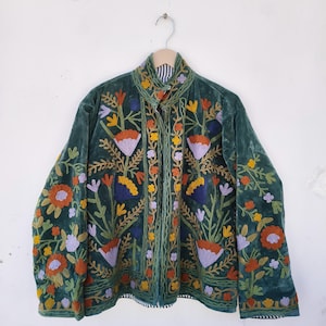 May include: A dark green velvet jacket with colorful floral embroidery. The jacket features orange, yellow, purple, and blue flowers with green leaves and stems. The collar and cuffs have a striped pattern.
