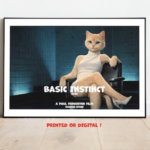 May include: A framed print featuring a cat in a white dress and heels, seated in a chair, with the text "BASIC INSTINCT 1992" and "A PAUL VERHOEVEN FILM SHARON STONE". The print is displayed on a wooden surface.