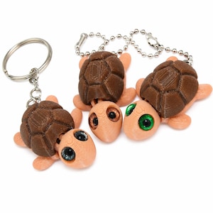 May include: A selection of turtle keyrings. The turtles feature brown, textured shells, peach-coloured bodies, and large, expressive eyes in various colours. One keyring has a silver ring, others have ball chains.