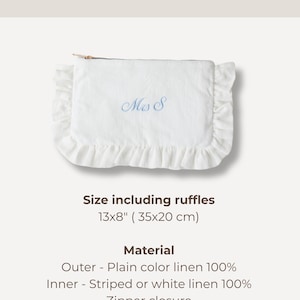 K&ouml;nnte beinhalten: Wei&szlig;e Leinen-Clutch mit R&uuml;schenkanten, bestickt mit "Ms S" in Blau. Die Clutch misst 35x20 cm inklusive R&uuml;schen. Sie hat einen Rei&szlig;verschluss und besteht aus 100 % einfarbigem Leinen au&szlig;en und gestreiftem oder wei&szlig;em Leinen innen.