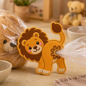 May include: A yellow and brown embroidered lion patch with a dark brown mane, pink cheeks, and a raised tail. The patch features a circular flower-shaped opening at the rear, through which a clear plastic bag is threaded and pulled through.