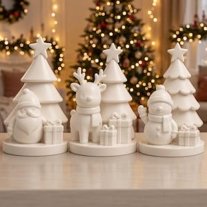 Può includere: Tre decorazioni da tavolo in ceramica bianca su basi circolari. La prima presenta una figura di Babbo Natale e un albero di Natale con una stella. La seconda mostra una renna e un albero. La terza mostra un pupazzo di neve e un albero, tutti con regali.