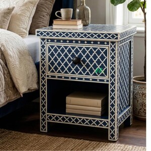 Könnte beinhalten: Nachtschrank in Marineblau mit weißem geometrischen Muster. Der Nachttisch hat eine Schublade mit schwarzem Knopf und ein offenes Regal. Oben stehen eine Tasse und Bücher.