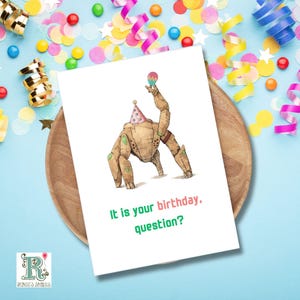 May include: A white greeting card featuring a brown, mechanical robot character wearing a colourful polka-dot party hat and holding a small maraca. The text on the card reads, "It is your birthday, question?" in green and pink lettering.
