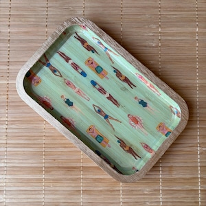 May include: A rectangular wooden tray with rounded corners featuring a light green interior surface decorated with a repeating pattern of small figures swimming and lounging on floats in various colorful swimsuits and beach attire.