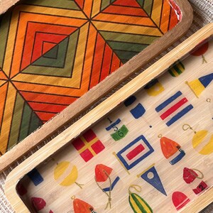 May include: Two rectangular wooden trays. One tray features a geometric pattern in orange, yellow, green, and black. The other tray has a nautical theme with colorful buoys, flags, and other maritime symbols.