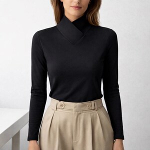 May include: A black long-sleeve top with a unique, angular neckline. The top is paired with beige pleated trousers. The outfit is simple and elegant, suitable for various occasions.