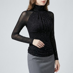 Könnte beinhalten: Schwarzes Langarm-Top mit hohem Ausschnitt und transparentem Mesh-Overlay. Das Top ist mit kleinen, funkelnden Akzenten verziert. Das Design hat eine geraffte Brustpartie und eine figurbetonte Silhouette.