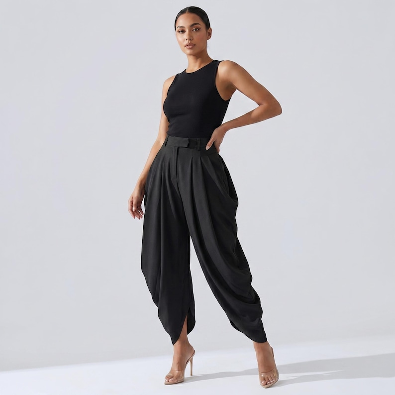 May include: A black sleeveless top and matching black trousers. The trousers have a unique draped design with a high waist and a belt. The model is wearing clear high heels. The outfit is set against a plain white background.