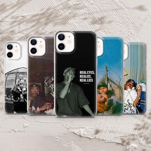 Pode incluir: Cinco capas transparentes para smartphone com várias impressões fotográficas de artistas de hip-hop. A capa central exibe um retrato a preto e branco de Tupac Shakur com o texto "REAL EYES, REALIZE, REAL LIES" impresso a branco.