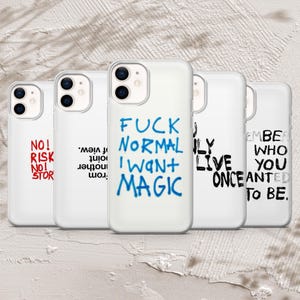 Pode incluir: Uma coleção de capas de telefone brancas com vários designs de texto. Uma capa tem as palavras "FUCK NORMAL I WANT MAGIC" em azul. Outras capas apresentam frases como "NO! RISK NO! STOR" em vermelho e "REMEMBER WHO YOU ONCE WANTED TO BE" em preto.