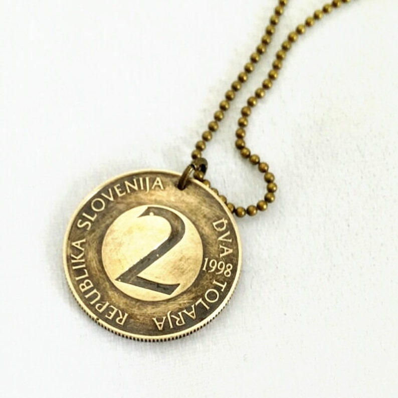 May include: A gold-colored necklace with a Slovenian 2 Tolar coin pendant. The coin features the number "2" and the text "REPUBLIKA SLOVENIJA" and "DVA TOLARA 1998".