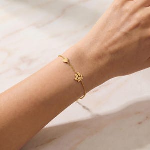 Puede incluir: Una delicada pulsera dorada con un dije de coraz&oacute;n y un dije de huella de pata. El dije de huella de pata tiene una peque&ntilde;a inscripci&oacute;n. La pulsera se lleva en la mu&ntilde;eca.