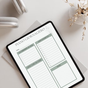 May include: A digital planner with the text "PIANO GIORNALIERO" and sections for daily priorities, appointments, to-do lists, and notes. The planner is on a tablet with a black frame, and a pair of white headphones is visible.