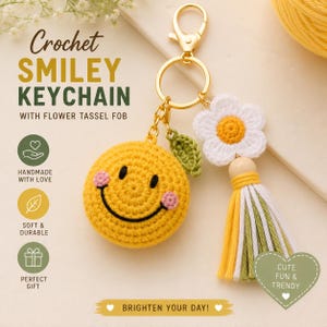 Op de afbeelding: Een gele gehaakte smiley-sleutelhanger met een klein groen blaadje, een wit-gele bloem en een veelkleurige kwast in geel, wit en groen. De sleutelhanger is voorzien van een goudkleurige metalen ring en een sluiting voor bevestiging.