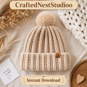 May include: A beige knitted beanie hat with a ribbed design and a pom-pom on top. The hat has a small brown tag and is displayed on a neutral surface. The image also includes text that says "CraftedNestStudioo" and "Instant Download".