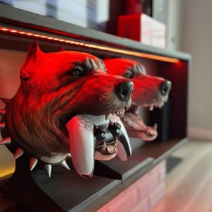 May include: A distinctive dog head sculpture in shades of brown and tan, holding a white and black game controller. The sculpture features a spiked collar and sits on a dark wooden shelf with red lighting.