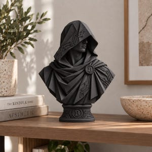 Könnte beinhalten: Eine mattschwarze Büste einer Kapuzenfigur mit geometrischen, Low-Poly-Stil-Merkmalen. Der Umhang ist mit Leiterplattenmustern und einer runden Bitcoin-Logo-Brosche verziert. Der Sockel zeigt ein kreisförmiges Bitcoin-Symbol im Relief.