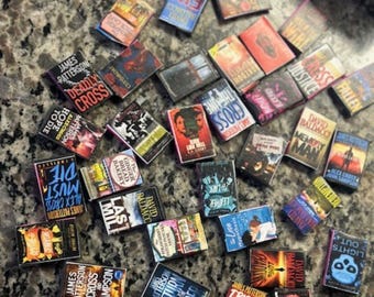 May include: A collection of miniature books with various titles and authors, including James Patterson and David Baldacci. The book covers feature a range of colors and designs, with titles like "Deadly Cross" and "Lights Out".
