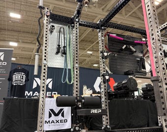 May include: A black and silver steel power rack with a REP branded adjustable bench, featuring a vertical pegboard attachment, a barbell holder, and a pulley system. The structure includes numbered uprights and various gym accessories.