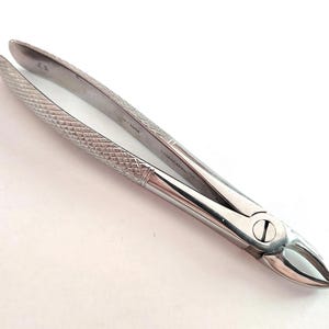 May include: A pair of stainless steel dental extraction forceps with a textured, cross-hatched diamond pattern on the long, slender handles. The tool features a hinged pivot point with a visible screw and curved, pointed tips for gripping.