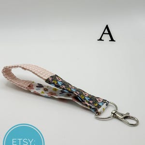 Könnte beinhalten: Ein Schlüsselband aus Stoff mit Blumen- und Tupfenmuster. Das Schlüsselband ist an einem silberfarbenen Metallverschluss befestigt. Das Etsy-Logo befindet sich in der unteren linken Ecke.