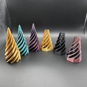Puede incluir: Seis objetos decorativos en forma de espiral en oro, turquesa, morado, amarillo, negro y rosa. Cada uno tiene una base hexagonal y un diseño en espiral, creando una estética única.