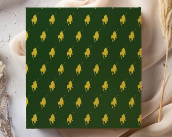 May include: A square, dark green canvas with a repeating pattern of gold-colored equestrian figures. The figures are evenly spaced across the surface. The canvas is displayed on a neutral background with floral and fabric elements.