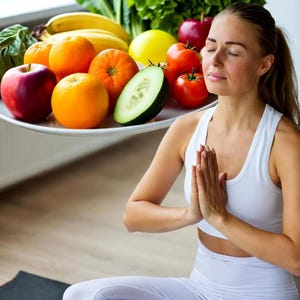 Può includere: Una donna in abbigliamento sportivo bianco medita con le mani giunte in preghiera. Un piatto contiene un assortimento colorato di frutta e verdura fresca, tra cui arance, mele, pomodori e lattuga. La scena suggerisce un focus sulla salute e il benessere.