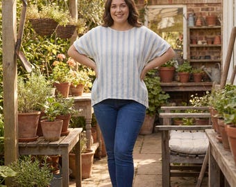 Könnte beinhalten: Eine Frau in einem hellblau-weiß gestreiften Oberteil und einer blauen Jeans steht in einem Garten. Das Oberteil hat einen Rundhalsausschnitt und kurze Ärmel. Der Garten hat Topfpflanzen, Holzmöbel und ein Backsteingebäude.