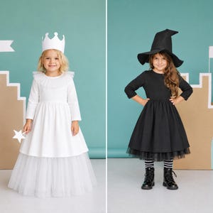 May include: Two children in costumes. One wears a white dress with a crown and holds a star-shaped wand. The other wears a black dress, witch hat, and boots. Both are in front of a light blue backdrop with castle-like cutouts.