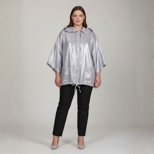 May include: A silver metallic hooded jacket with a drawstring waist and button closure. The jacket is paired with black pants and gray heels. The outfit is a modern, stylish ensemble.