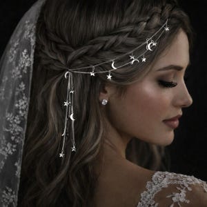 Puede incluir: Un tocado plateado con estrellas y lunas crecientes colgantes. El delicado diseño de cadena se lleva en el pelo, con un peinado trenzado y un velo de encaje en el fondo. Un accesorio nupcial.