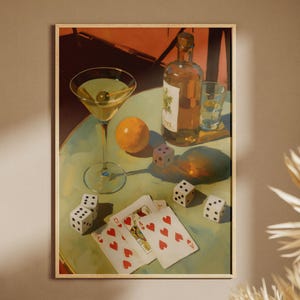 May include: A framed still life painting featuring a martini with an olive, a bottle of wine, a glass of water, an orange, playing cards, and dice on a green table. The painting has a vintage aesthetic with warm lighting.
