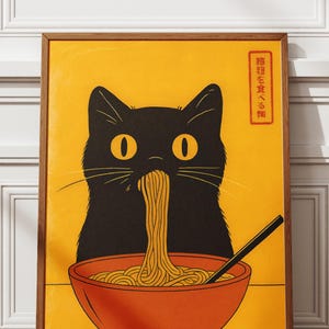 May include: A framed poster featuring a black cat eating noodles from an orange bowl. The cat has large yellow eyes and is set against a yellow background. Japanese text is in the upper right corner. The poster has a wooden frame.