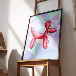 May include: Framed art print featuring a red balloon dog illustration. The dog is set against a geometric background of pastel colors, including purple, blue, and green. The artwork is displayed on a wooden stand.