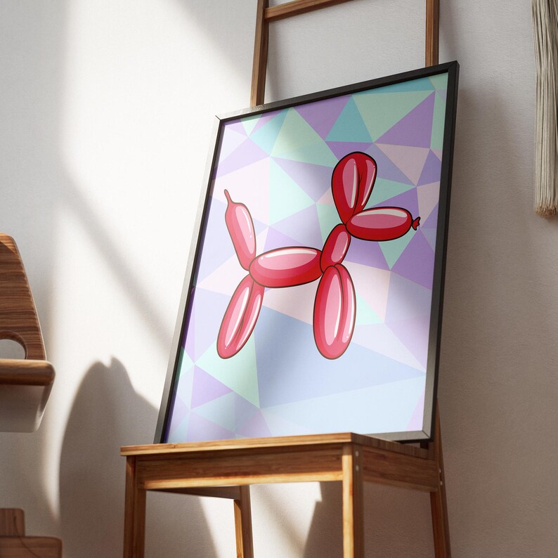 May include: Framed art print featuring a red balloon dog illustration. The dog is set against a geometric background of pastel colors, including purple, blue, and green. The artwork is displayed on a wooden stand.