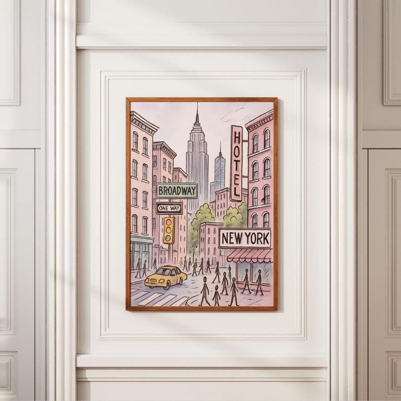 May include: A framed art print depicting a New York City street scene. The illustration features buildings, street signs reading "Broadway", "One Way", and "New York", a yellow taxi, and pedestrians. The Empire State Building is visible in the background.