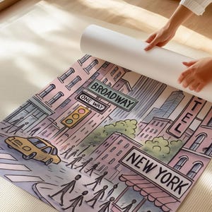 May include: A colorful illustration of a New York City street scene, featuring Broadway street signs, a yellow taxi, and pedestrians. The artwork is being unrolled, revealing the full cityscape.