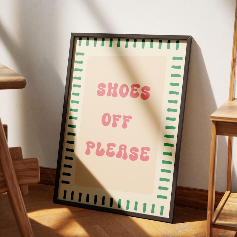 May include: A rectangular framed wall art print featuring a light beige background with a border of short green horizontal lines. The text SHOES OFF PLEASE is printed in the center in a bold, rounded, pink font with a wavy, retro-inspired style.