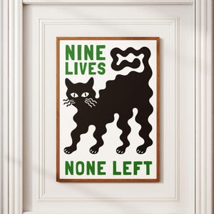 以下が含まれることがあります： 黒猫のイラストが描かれた額入りのアートプリント。猫の体と尾は波線で描かれています。「NINE LIVES」と「NONE LEFT」の文字が猫の上下に緑色で書かれています。木製のフレームに入っています。