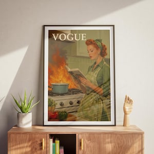 Peut inclure: Reproduction d'une couverture de magazine Vogue de style vintage encadr&eacute;e. L'image montre une femme lisant un livre de cuisine dans une cuisine en feu. Le logo Vogue est en haut. Palette de couleurs : verts, oranges et blancs.