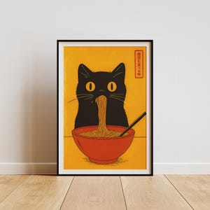 May include: A framed art print featuring a black cat eating noodles from a red bowl. The cat has large yellow eyes and is set against a yellow background. The print includes Japanese text in a red rectangle.
