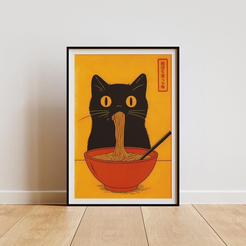 May include: A framed art print featuring a black cat eating noodles from a red bowl. The cat has large yellow eyes and is set against a yellow background. The print includes Japanese text in a red rectangle.