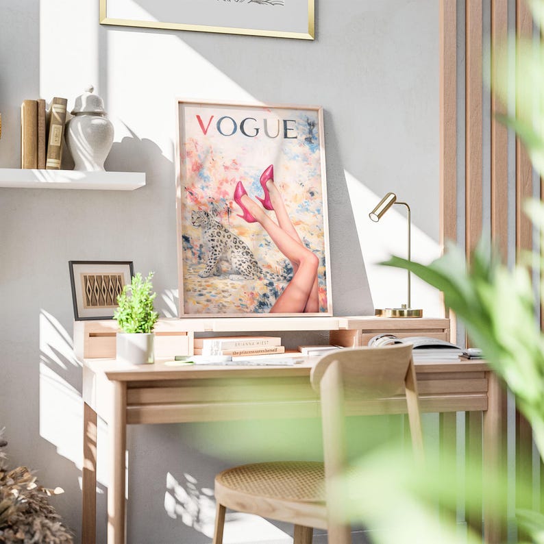 Op de afbeelding: Een ingelijste kunstafdruk van de "VOGUE" magazinecover met een luipaard en benen in roze hakken. De print wordt weergegeven op een houten bureau met een kleine lamp, boeken en een stoel. Een kleine plant en decoratieve items zijn ook zichtbaar.